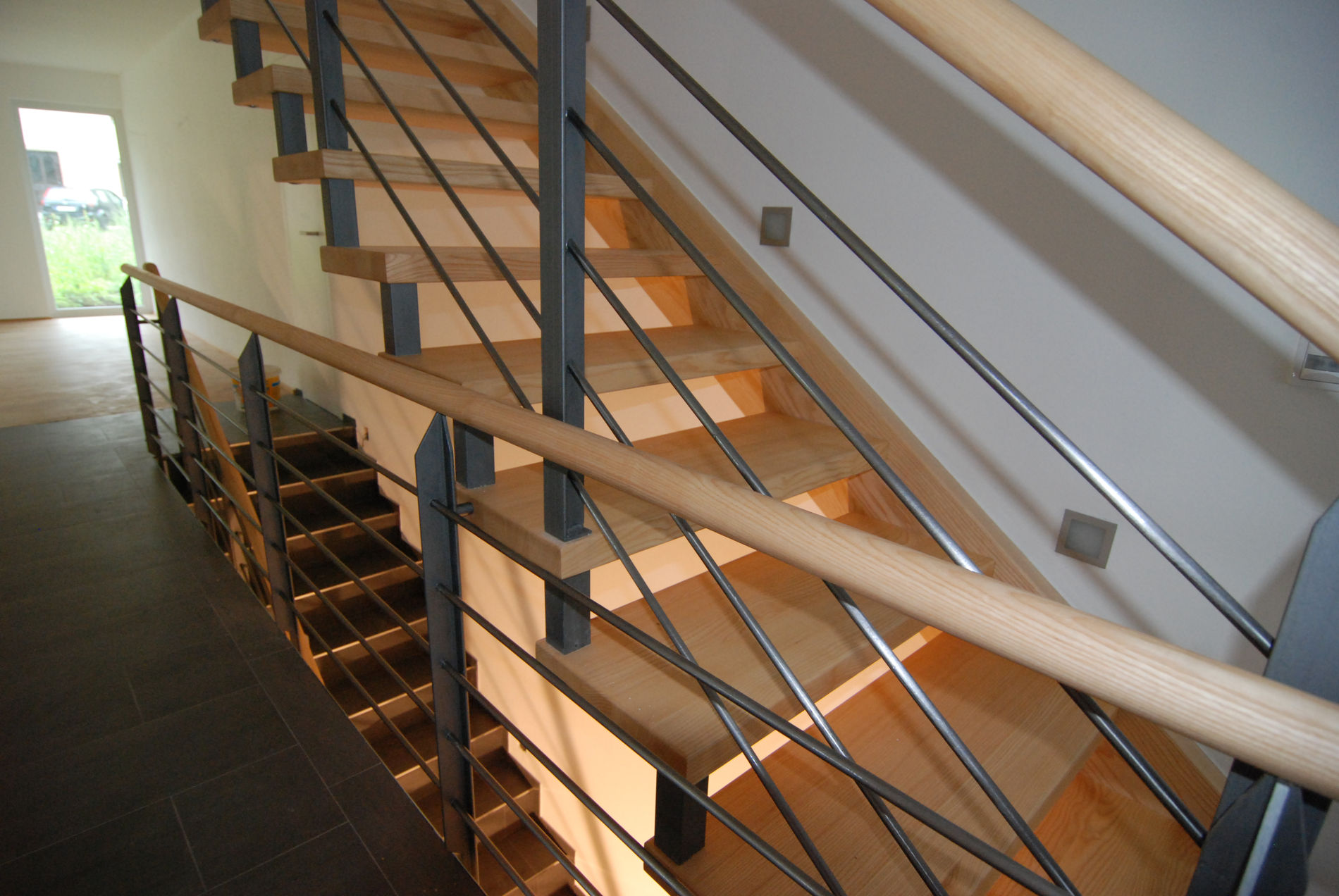 Moderne Holztreppe mit Edelstahlgeländer und Seilgeländer in einem hellen Treppenhaus, Sicht von oben auf die Stufen.