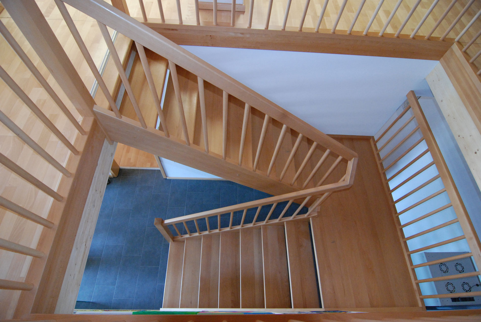 Blick von oben auf eine hölzerne Wendeltreppe mit offenen Stufen und einem Geländer aus vertikalen Holzstäben, die eine moderne Innenarchitektur widerspiegelt.